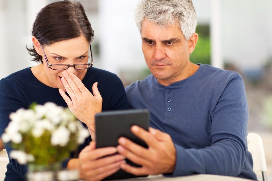 middle aged couple reading shocking news on tablet computer