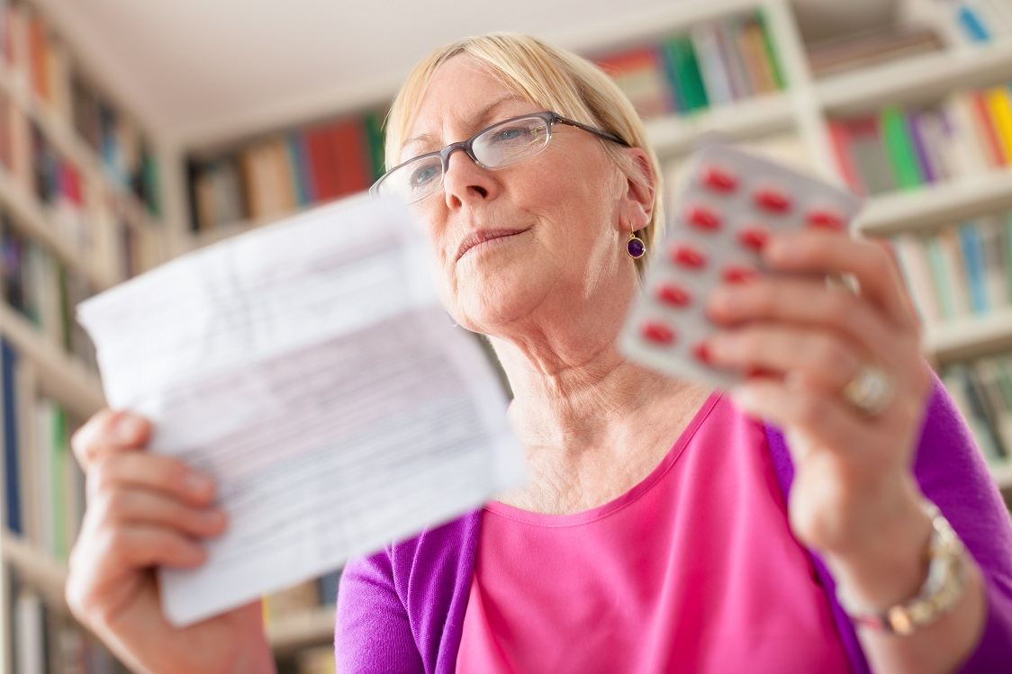 Elderly caucasian woman with medicine and reading drug prescription. Low angle view