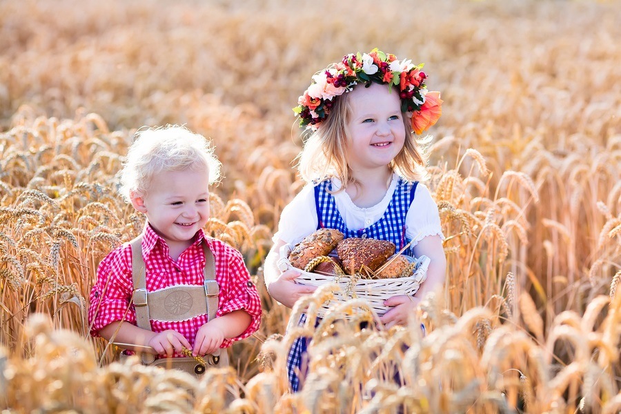 Kids in traditional Bavarian costumes in wheat field. German children eating bread and pretzel during Oktoberfest in Munich. Brother and sister play outdoors during autumn harvest time in Germany.