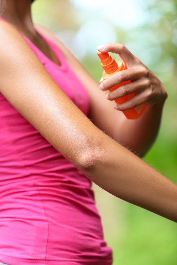 Mosquito repellent. Woman spraying insect repellents on skin outdoor in nature using spray bottle in forest.