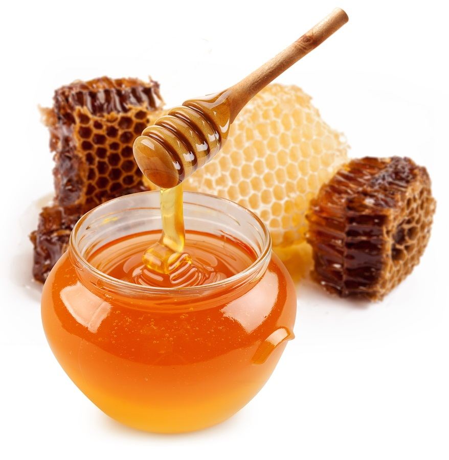 Pot of honey and wooden stick are on a table.