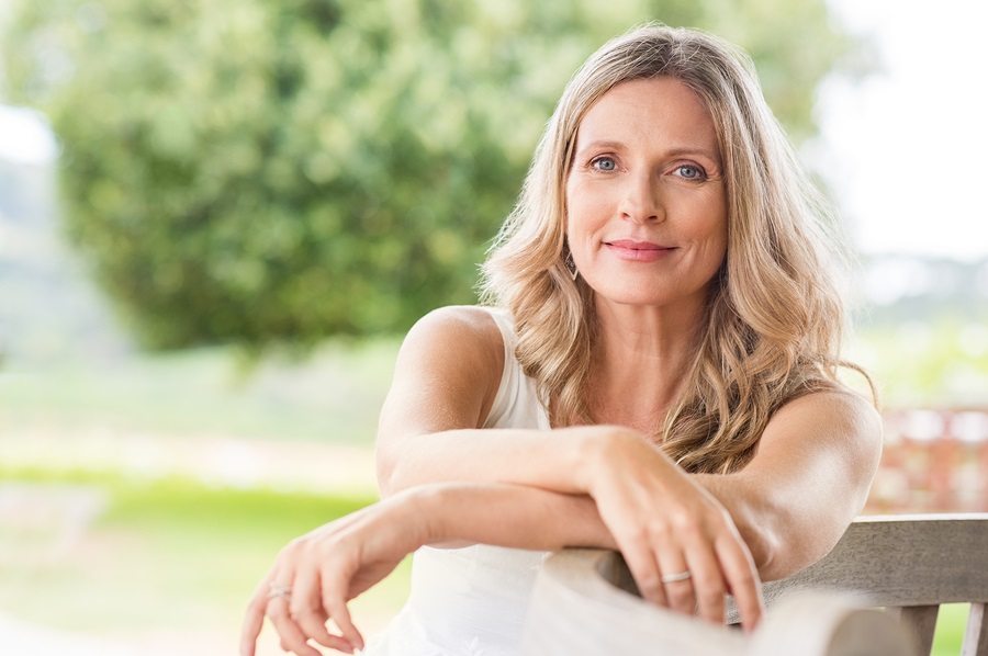 Happy senior woman relaxing on bench in the lawn. 