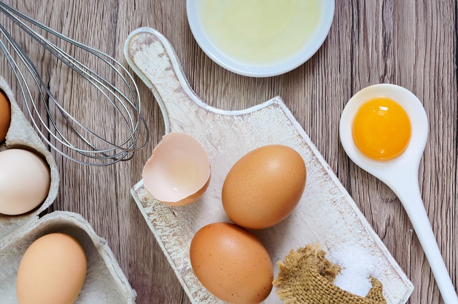 Fresh farm eggs on a wooden rustic background. Separated egg white and yolks, broken egg shells. Whipping eggs with whisk. Preparation of food from chicken eggs. The top view. View from above.