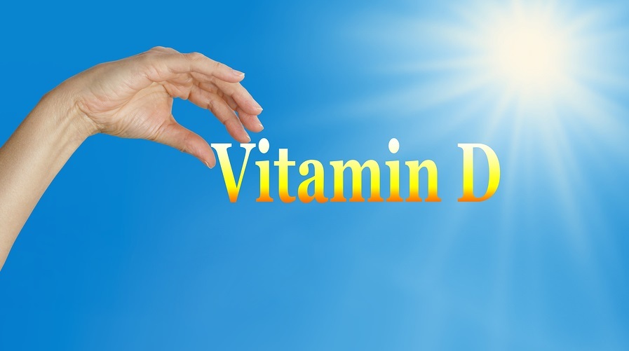 Sunshine and blue sky background with the word Vitamin D and a female hand poised to pick the D image