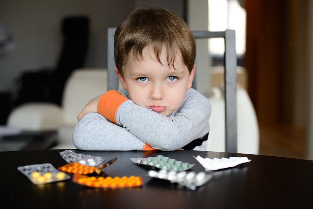 sad preschooler sitting at the table with pills
